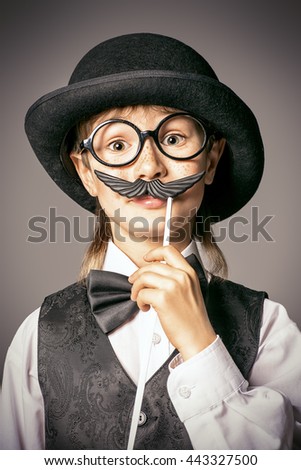 Funny boy in a bowler hat and spectacles plays with false mustache. Generation concept. Children fashion. 