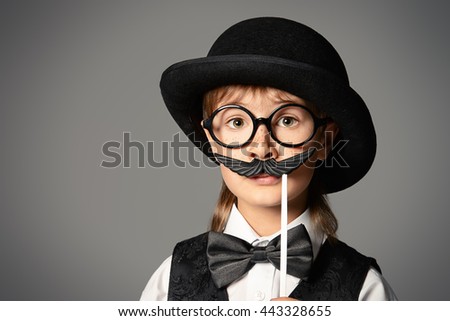 Funny boy in a bowler hat and spectacles plays with false mustache. Generation concept. Children fashion. 