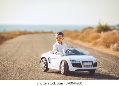 Funny boy car driver with the steering wheel. year-old boy in a white shirt in a red toy car in the street. Little boy driving big toy car and having fun, outdoors. Young kid portrait with toy car - Shutterstock ID 390044200