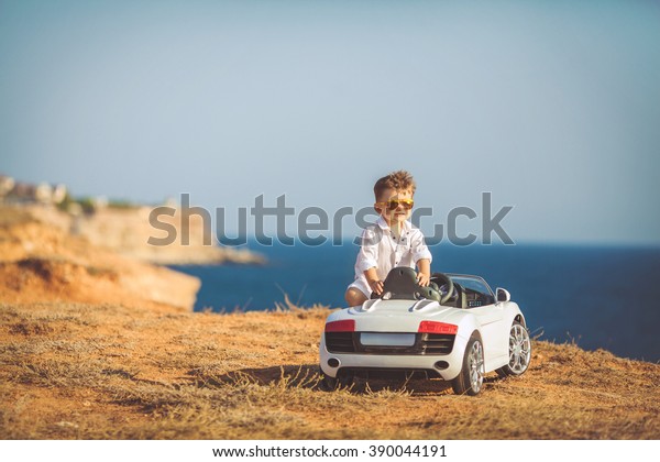 Funny boy car driver with the steering wheel.
year-old boy in a white shirt in a red toy car in the street.
Little boy driving big toy car and having fun, outdoors. Young kid
portrait with toy car