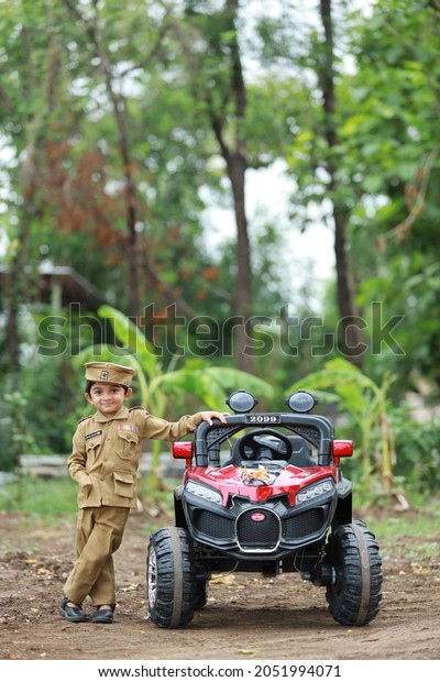 Funny boy car driver. year-old boy in a police uniform\
in a red toy car outdoors. Young kid portrait with toy car, Indian\
police uniform 