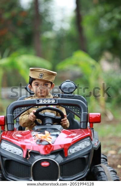 Funny boy car driver. year-old boy in a police uniform\
in a red toy car outdoors. Young kid portrait with toy car, Indian\
police uniform 