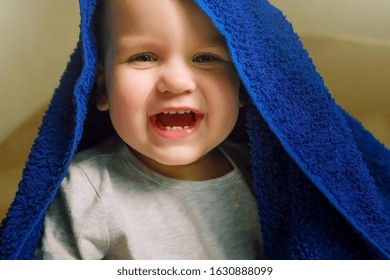 Funny Boy Kid With A Color Classic Blue Towel On His Head. Baby After Bathing On The Bed.