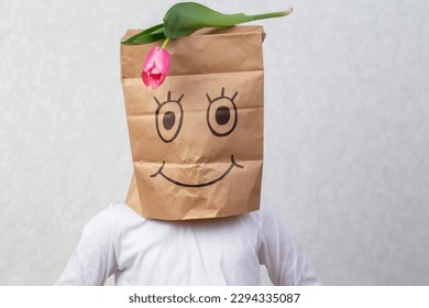 A funny boy put paper bag and painted smile his head   put tulip it  The concept an anonymous gift 
