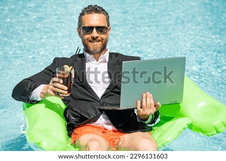 Funny business man in a business suit floating in the water in the pool. Remote work. Crazy freelancer. Business and summer. Business man drink summer cocktail and using laptop in pool.