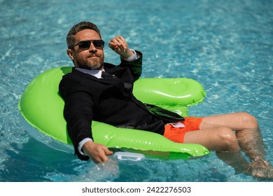 Funny business man in a business suit works for a laptop standing in the water in pool. Remote work. Crazy freelancer. Business and summer. Business man working online with computer laptop in pool. - Powered by Shutterstock