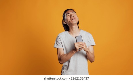 Funny carefree man singing songs on camera, using smartphone as microphone and fooling around. Confident young guy acting silly or funky, enjoying music and audio in studio.