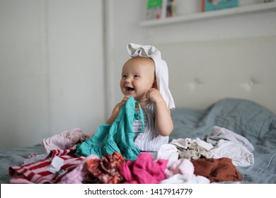 Funny Caucasian Baby 10 Months Playing With A Bunch Of Clothes, A Mess And Children, Motherhood And Mom Do Not Have Time, Rummaged At Home. Bright Bedroom Interior