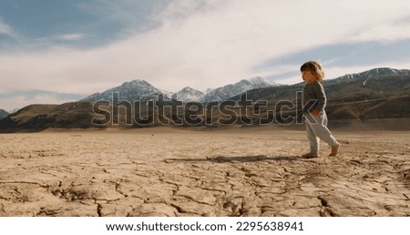  Funny caucasian baby boy running on deserted ground. Cracked soil land after erosions and desertification - ecology, save our planet concept 