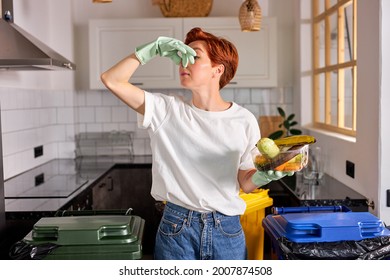 Funny caucasian female in casual wear throwing spoiled fruit into waste bins cans, caucasian redhead woman wrinkles face feeling the unpleasant smell of spoiled food, plugs the nose. copy space