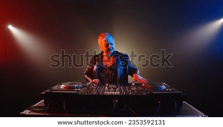Funny caucasian grandma in authentic outfit and makeup working as a cool dj in a nightclub, dancing and cheering at turntables 