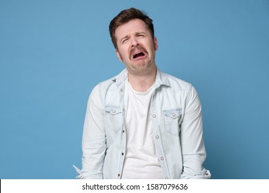 Funny caucasian man crying wipes tears losing his job. Studio shot on blue background.