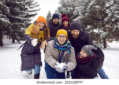 Funny cheerful group of friends having fun outdoors in park with snow in winter on beautiful frosty day. Man surrounded by friends is going to throw snow up. Concept of friendship and active life
