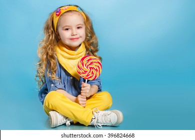Funny child with candy lollipop, happy little girl eating big sugar lollipop, kid eat sweets. surprised child with candy. isolated on bright background, studio. Beautiful little girl with lollipop