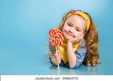 Funny Child With Candy Lollipop, Happy Little Girl Eating Big Sugar Lollipop, Kid Eat Sweets. Surprised Child With Candy. Isolated On Bright Background, Studio. Beautiful Little Girl With Lollipop