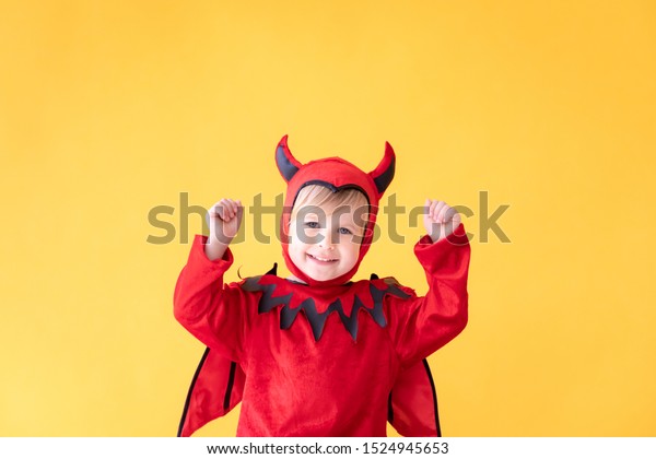 Funny child dressed devil\
costume against yellow background. Happy Halloween holidays\
concept