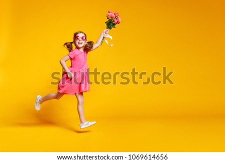 funny child girl runs and jumps with bouquet of flowers on a colored background
