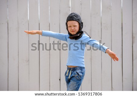 funny child inblue sweater and old pilot's helmet plays in fenced yard. boy dreams of becoming pilot