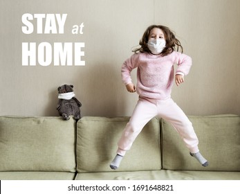 Funny Child Jumping On Couch During COVID-19 Corona Pandemic. Cute Baby Girl, Kid In Face Mask For Protection To Corona And Monkeypox Virus Plays Indoors. Stay At Home For Safe Live Due To Quarantine