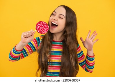 Funny child with lollipop over yellow isolated background. Sweet childhood life. Teen girl with yummy caramel lollipop, candy shop. Excited face, cheerful emotions of teenager girl.