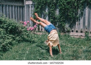 Funny child teenage girl doing cartwheel on backyard. Excited joyful kid playing outdoor. Happy lifestyle childhood and freedom spirit concept. Seasonal sport activity for children.