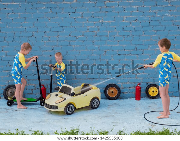 Funny children in boys\' bathing suits posing\
in front of camera with high-pressure car wash and toy yellow car\
and scooters. Brothers are trying to wash car. Concept educational\
games for preschoolers