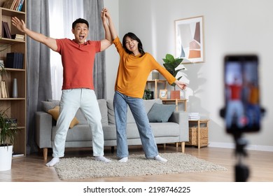 Funny Chinese Husband And Wife Recording Video For Social Media Or Personal Family Vlog, Holding Hands And Dancing In Front Of Camera, Using Modern Cell Phone On Tripod, Home Interior, Copy Space