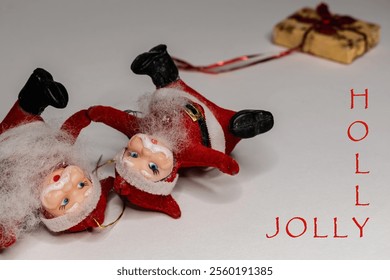 Funny christmas card design with small santa claus figures and christmas gift laying on the left side of a bright background, HOLLY JOLLY text - Powered by Shutterstock