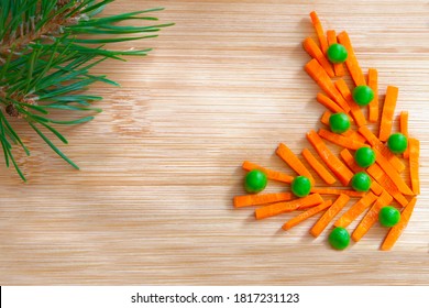 Funny Christmas Food Composition. Carrots And Peas Like A Christmas Tree Branch On A Wooden Board. New Year's Food, Celebration, Food Decoration. Top View. Flatlay