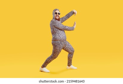 Funny Chubby Guy In Crazy Costume Having Fun In Modern Fashion Studio. Happy Cheerful Confident Fat Man Wearing Comfortable Leopard Pajamas Dancing Isolated On Yellow Background. Crazy Party Concept