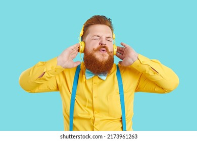 Funny Chubby Man Listening To Music. Happy Handsome Fat Guy With Ginger Beard And Handlebar Moustache Wearing Yellow Shirt, Blue Bowtie, Suspenders And Headphones Enjoying Songs And Singing Along