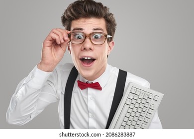 Funny Clever Male Programmer In Glasses And With White Keypad Looking At Camera With Astonishment On Gray Background In Studio