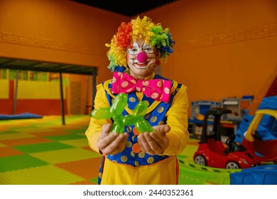 Funny clown holding balloon dog standing over playroom background - Powered by Shutterstock