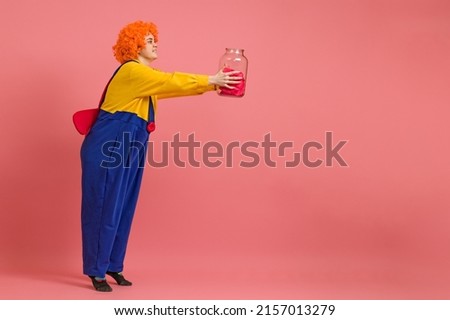 funny clown in a wig and a yellow-blue suit with a propeller on his back gives a jar of jam on a colored background with a place for text