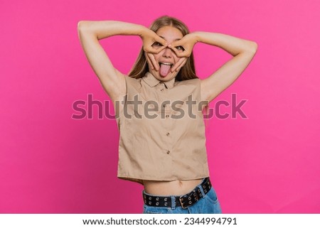 Funny comical playful young woman making silly facial expressions and grimacing, fooling around, showing tongue, idiotic expression. Girl isolated alone on pink studio background. People lifestyles