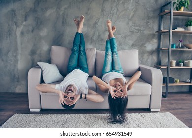 Funny couple with glasses gesturing is lying upside-down on the sofa at home. They are so cheerful, having fun together, go crazy, brother and sister