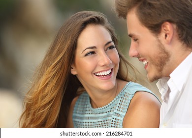 Funny couple laughing with a white perfect smile and looking each other outdoors with unfocused background             