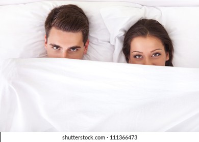 Funny Couple Lying In Bed With The Sheet Pulled Up Over Their Noses