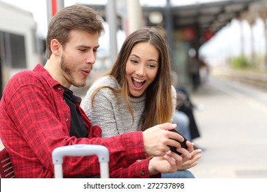 Funny couple playing games with a smart phone in a train station while they are waiting - Powered by Shutterstock