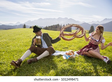 Funny couple smiling and playing in bavarian costumes for Oktoberfest wih beer mug and pretzel. Couple oktoberfest