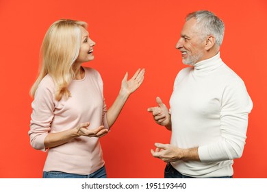 Funny Couple Two Friends Elderly Gray-haired Man Blonde Woman In White Pink Casual Clothes Standing Looking At Each Other Speaking Talking Isolated On Bright Orange Color Background Studio Portrait