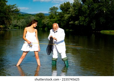 Funny couple of young pretty beauty woman and old fisherman standing in river with fishing rod. Old senior and girl fishing.