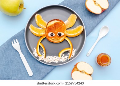 Funny crab face shape snack from pancake, orange,apples,honey on plate. Cute kids childrens baby's sweet dessert, healthy breakfast,lunch, food art on blue background,top view.
