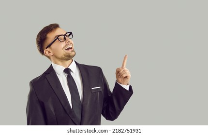 Funny Crazy Looking Entrepreneur Thinks Of A Great, Brilliant Business Idea. Studio Portrait Of A Happy Cheerful Man Isolated On A Solid Light Gray Background Smiling And Pointing His Index Finger Up