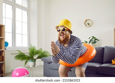 Funny crazy man with inflatable circle pretends to be swimming at home in living room. Absurd chubby guy in striped swimsuit having fun with circle for swimming at waist imagining that he is on beach.
