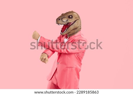 Funny crazy man with mask lizard or dinosaur head dancing isolated on pink background. Man in pink suit puts on animal's head and has fun during costume party. Creative concept for advertising.