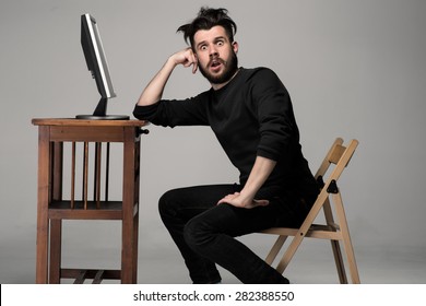 Funny and crazy man using a computer on gray background. Concept of surprise and indignation