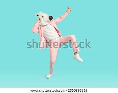 Funny crazy man wearing horse head mask dancing. Full length shot of eccentric creative guy in pastel pink suit dancing and having fun over isolated on light blue studio background