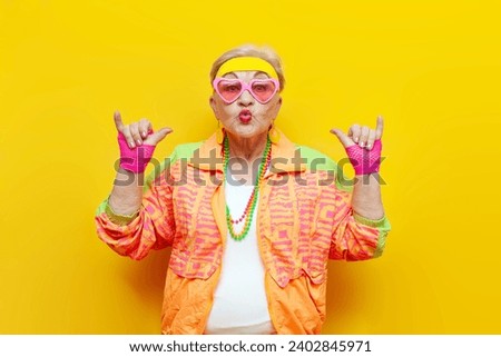 funny crazy old granny in sports hipster clothes shows youth gesture on yellow isolated background, elderly woman active lifestyle