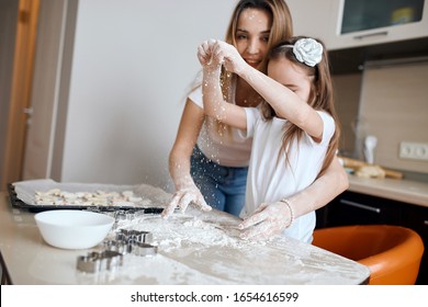 Funny Crazy Woman And Her Kid Spilling The Flour On The Kitchen Table. Close Up Photo. Little Girl With Raised Arms Throwing Flour On The Table